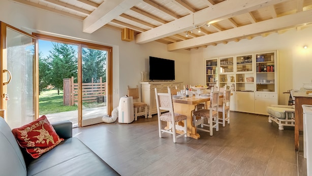 A spacious living area with a large sliding glass door leading to a garden, a dining area with a wooden table and chairs, and a kitchen with open shelving. - Mugello House With Pool (Vicchio)