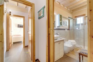 Quarto com estrutura de madeira, uma cama, banheiro com chuveiro e pia.