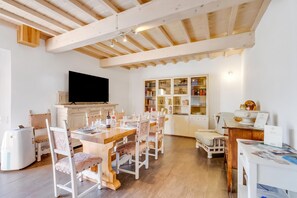 Un amplio salón con una mesa de comedor lista para cuatro personas, un televisor montado en la pared y una estantería llena de libros y objetos decorativos.