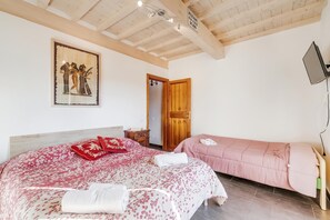 A bedroom with two beds, a wooden ceiling, a painting on the wall, and a television mounted on the wall. - Mugello House With Pool (Vicchio)
