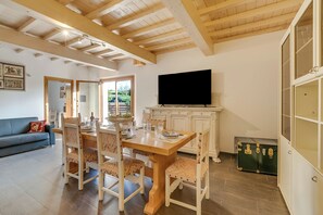 A dining area with a wooden table and chairs, a television, and a green suitcase. - Mugello House With Pool (Vicchio)