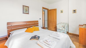 Una cama bien hecha con cabecera de madera, un sillón floral y un aparador de madera.