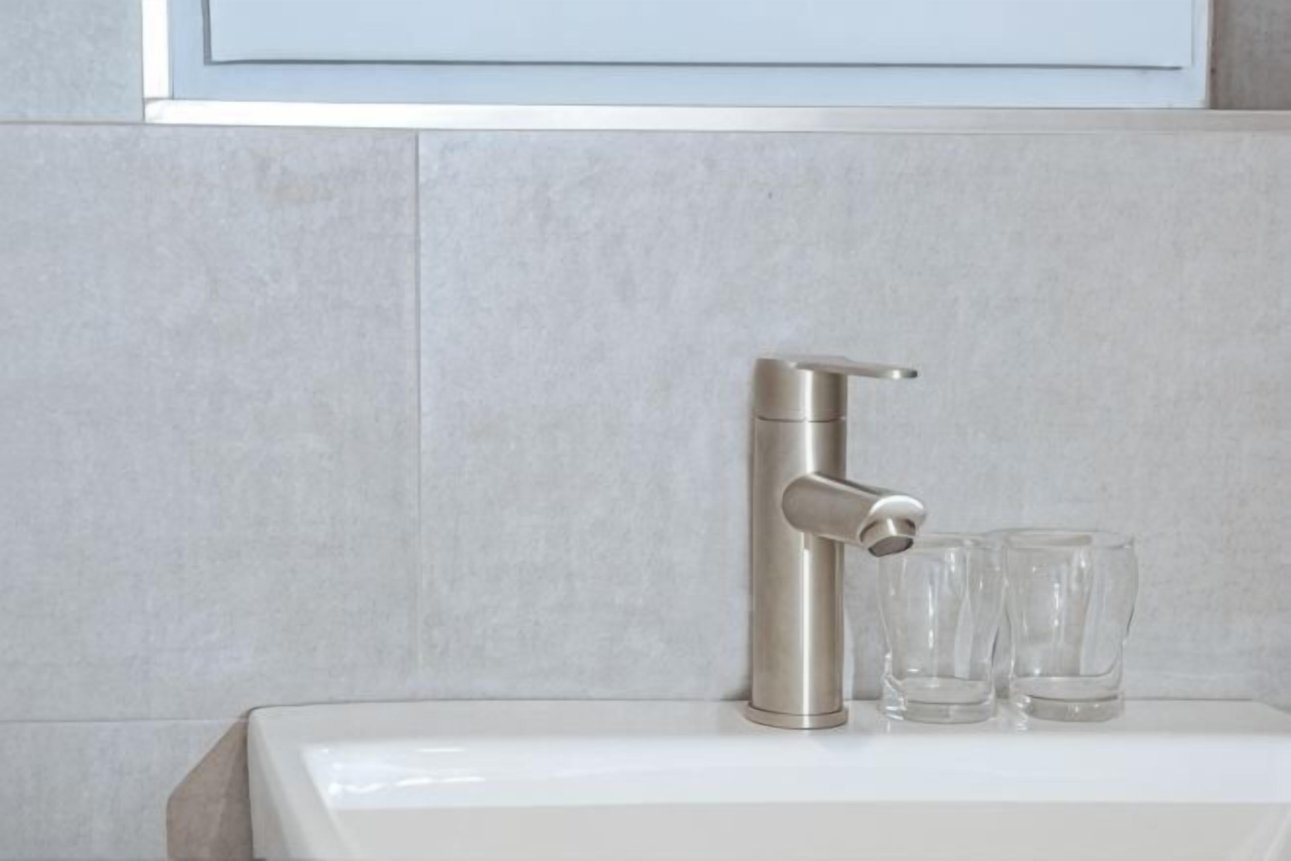 A bathroom with a modern faucet and two clear glasses on the sink.