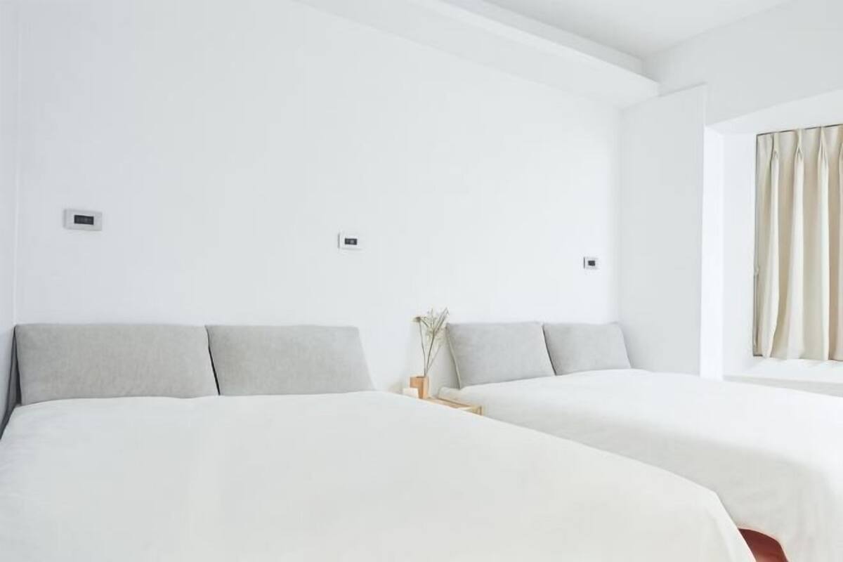Quarto de hotel com duas camas, paredes brancas e uma janela com cortinas.