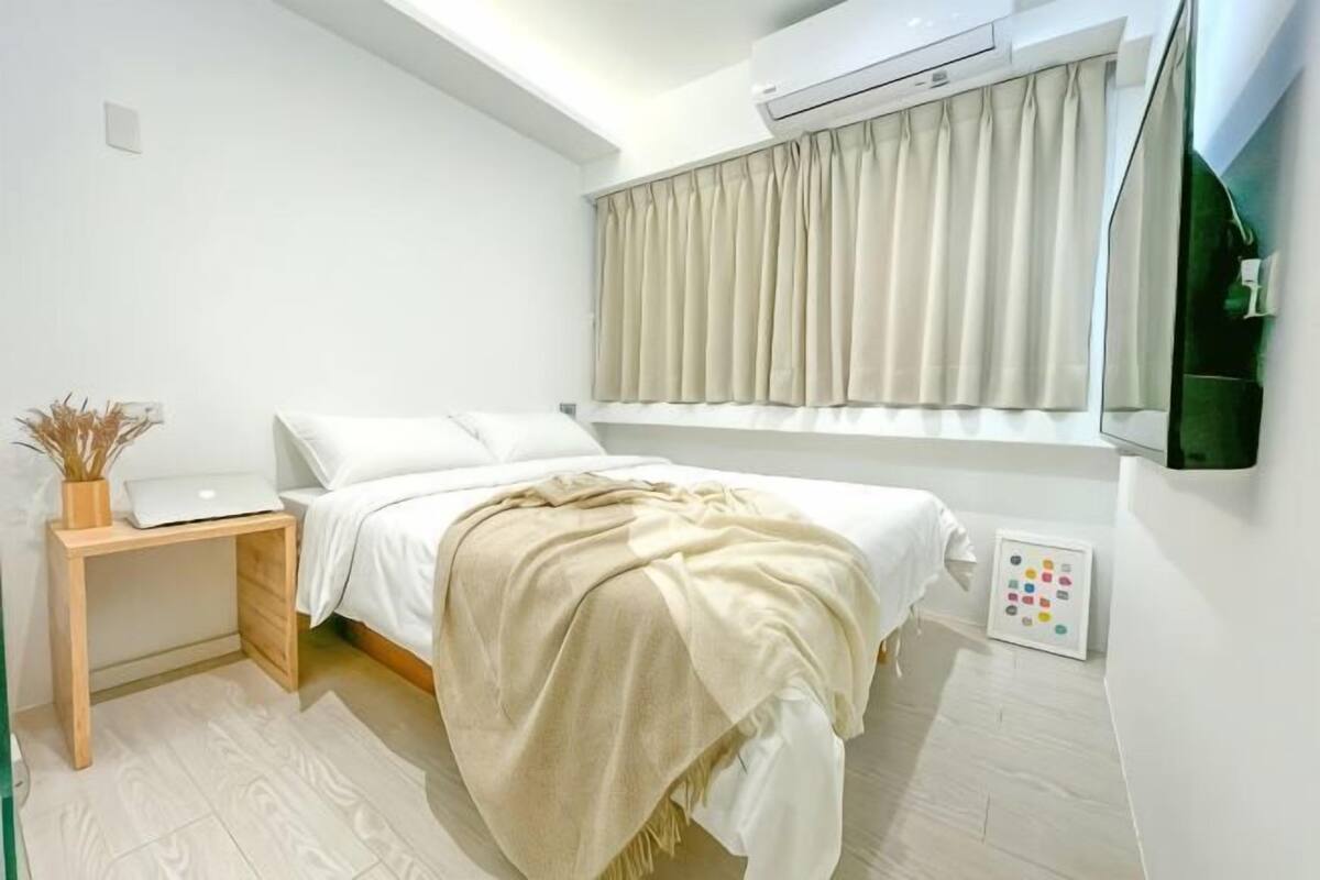 Um quarto com cama, mesa de cabeceira, luminária e janela com cortinas.