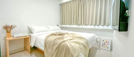 A bedroom with a bed, bedside table, lamp, and window with curtains.