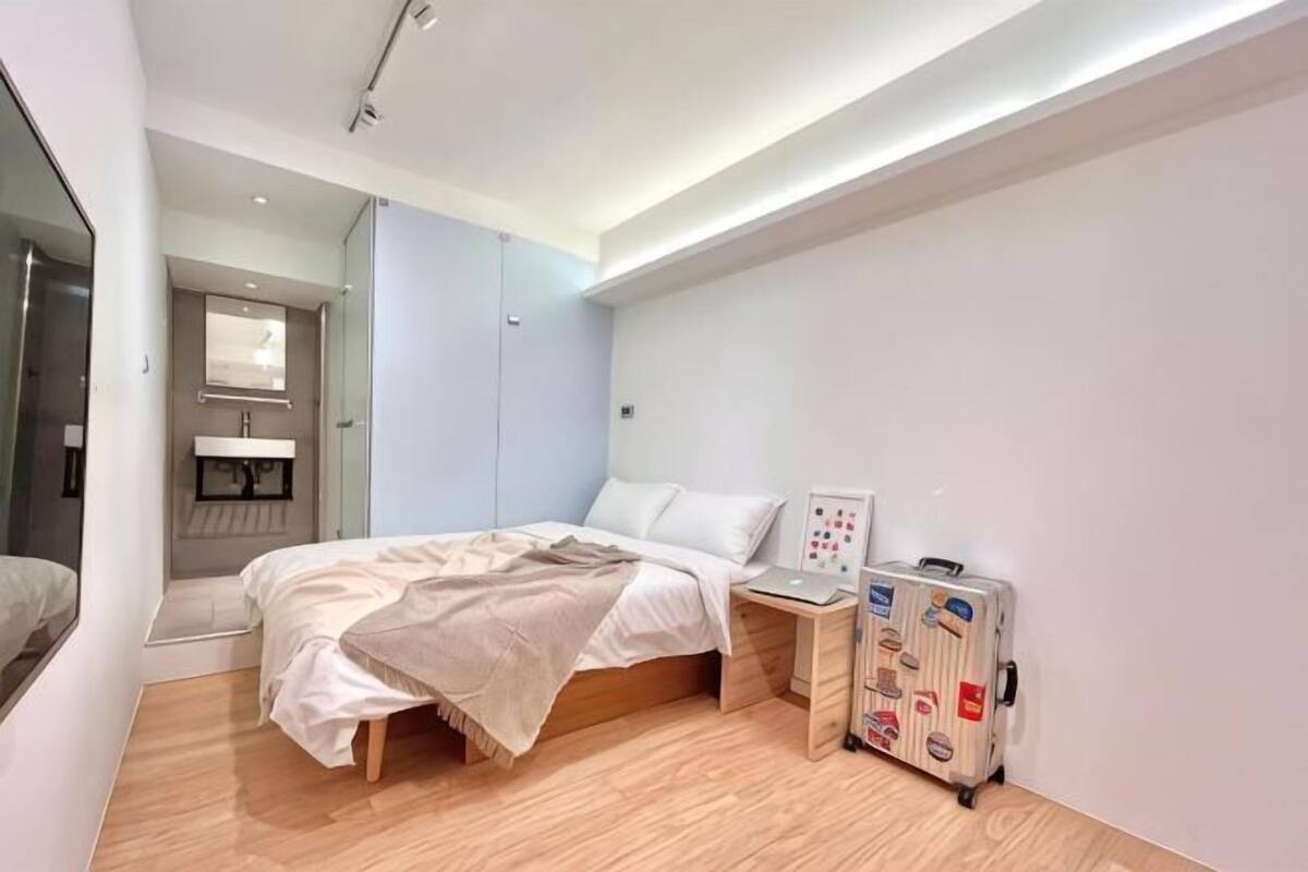 Quarto com cama, mesa de cabeceira e mala.