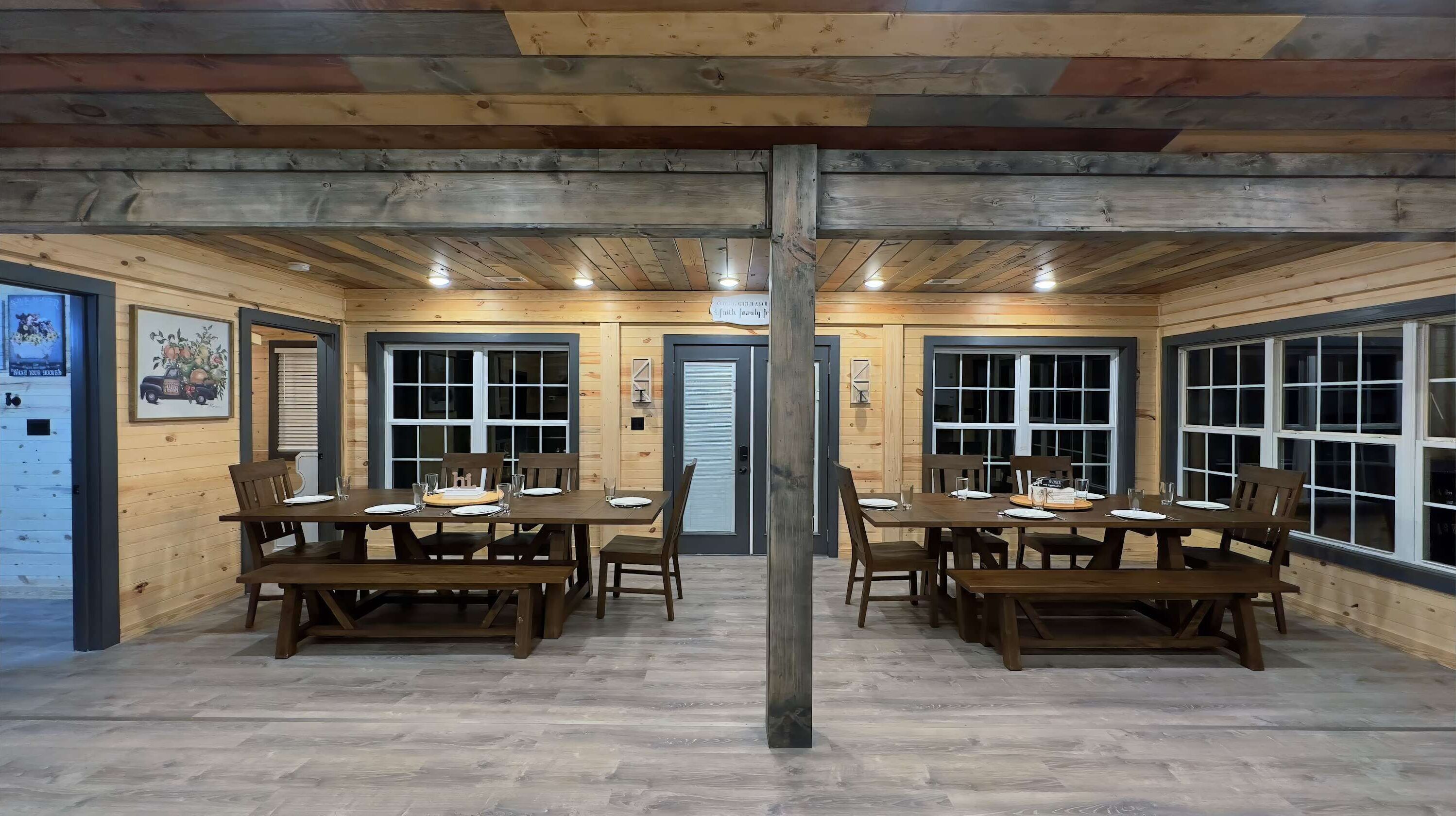 Een eetruimte met houten tafels en stoelen, grote ramen en een centrale houten balk.