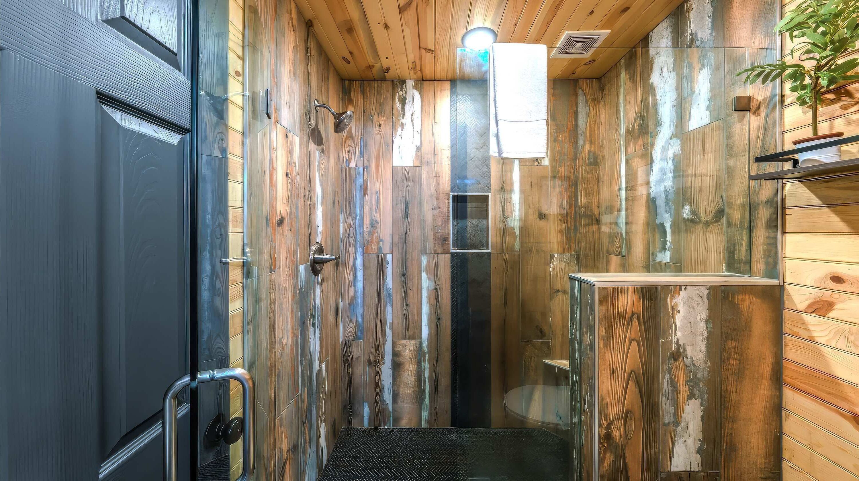 Un baño estrecho con paredes de madera, una puerta negra, un ventanal pequeño y una planta en maceta.