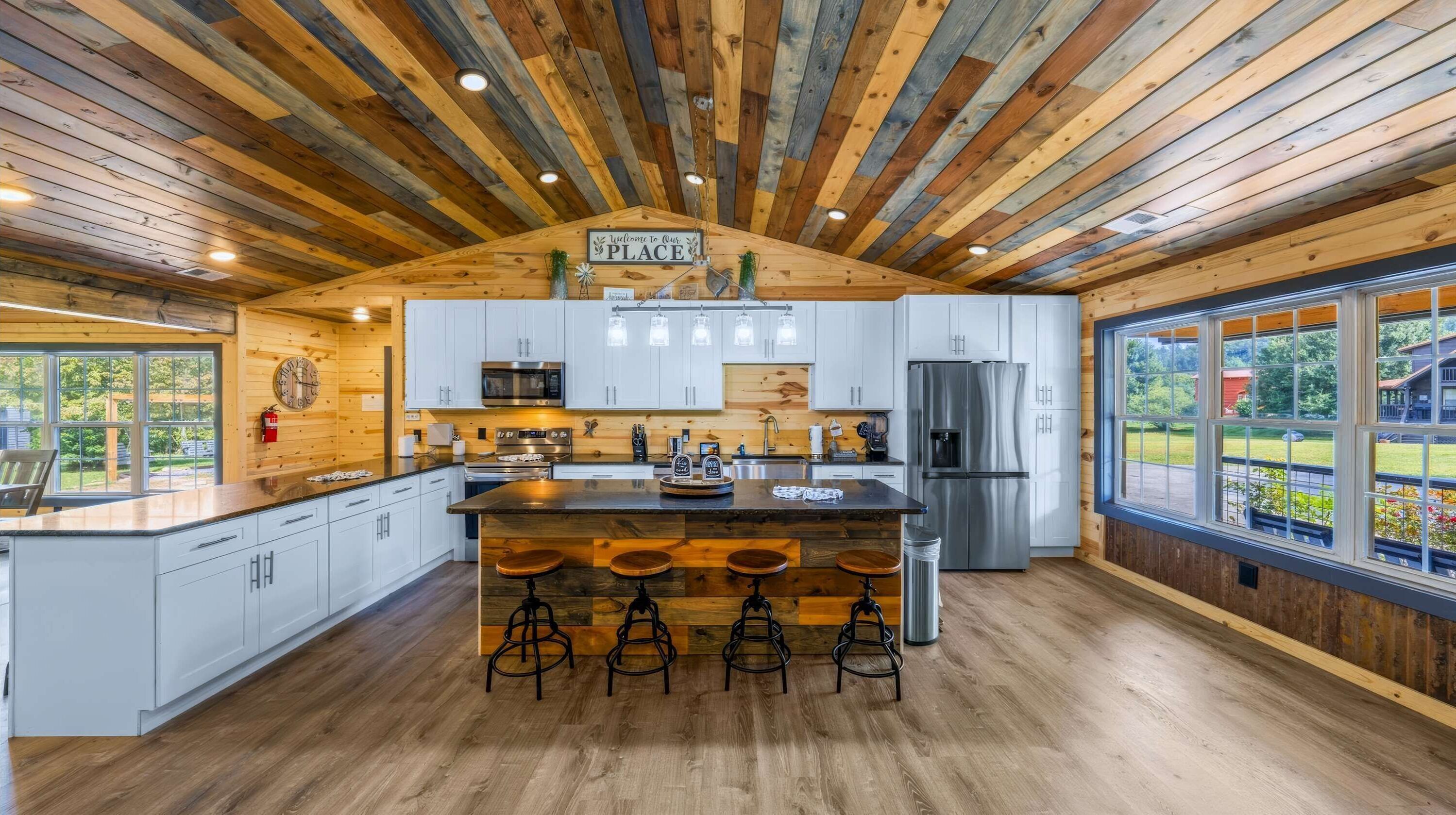 Una cocina moderna con armarios blancos, una isla central con taburetes, electrodomésticos de acero inoxidable y techo de madera.