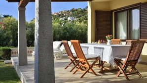 Eine Terrasse im Freien mit Tisch und Stühlen, umgeben von Steinsäulen und Blick auf eine Hügellandschaft.