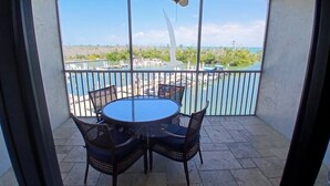 A balcony with a round table and four chairs, a ceiling fan, and a view of a marina with boats. - Charming bayside condo in south seas resort Captiva for a relaxing getaway (Captiva)