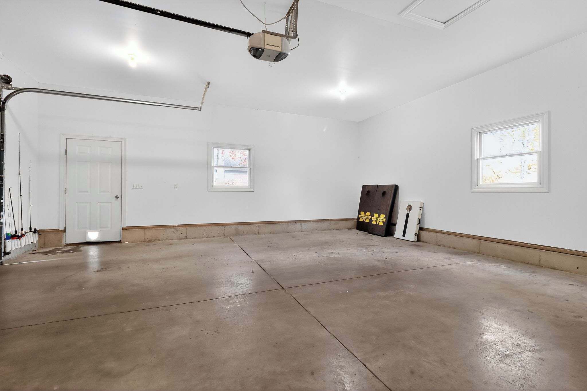 A spacious, empty room with a concrete floor, white walls, and two windows.