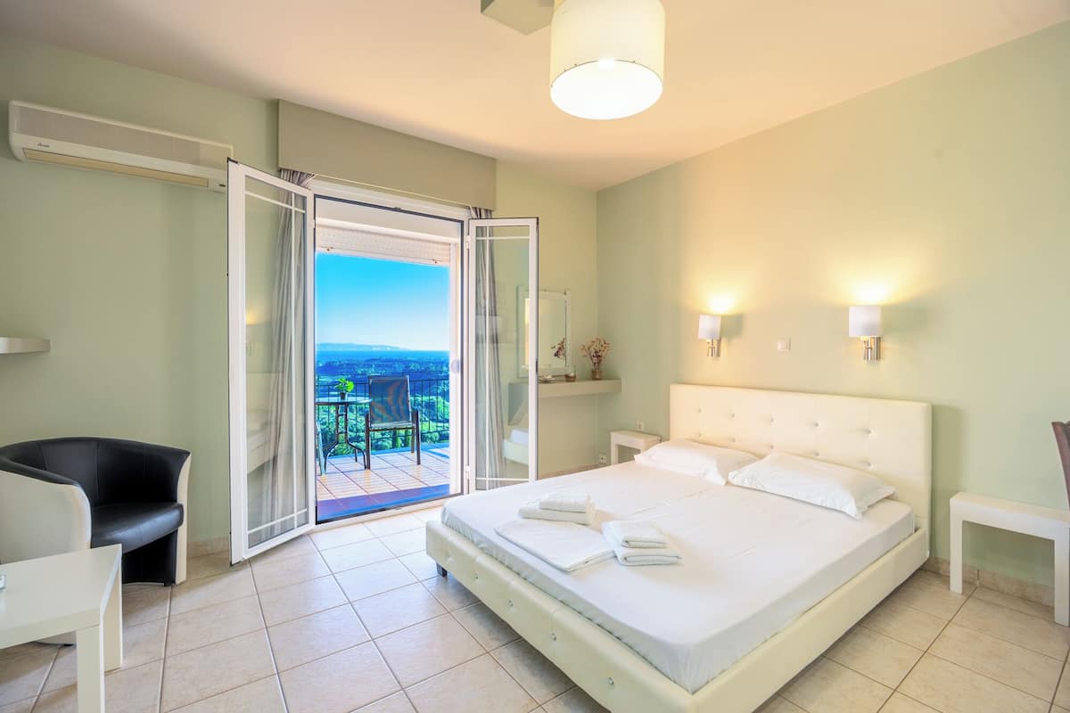 A bedroom with a bed, a chair, a bedside table, a nightstand, a window, and a view of the outdoors.