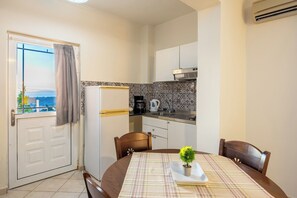 Une cuisine compacte équipée d’un réfrigérateur, d’une cuisinière et d’un évier. Une table à manger avec des chaises se trouve au premier plan.
