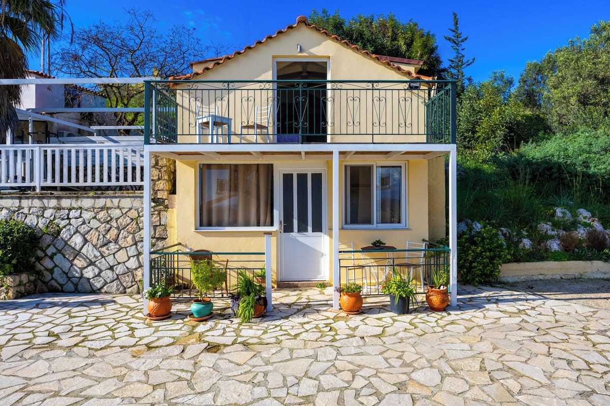 A two-story building with a balcony, stone-paved entrance, and potted plants.