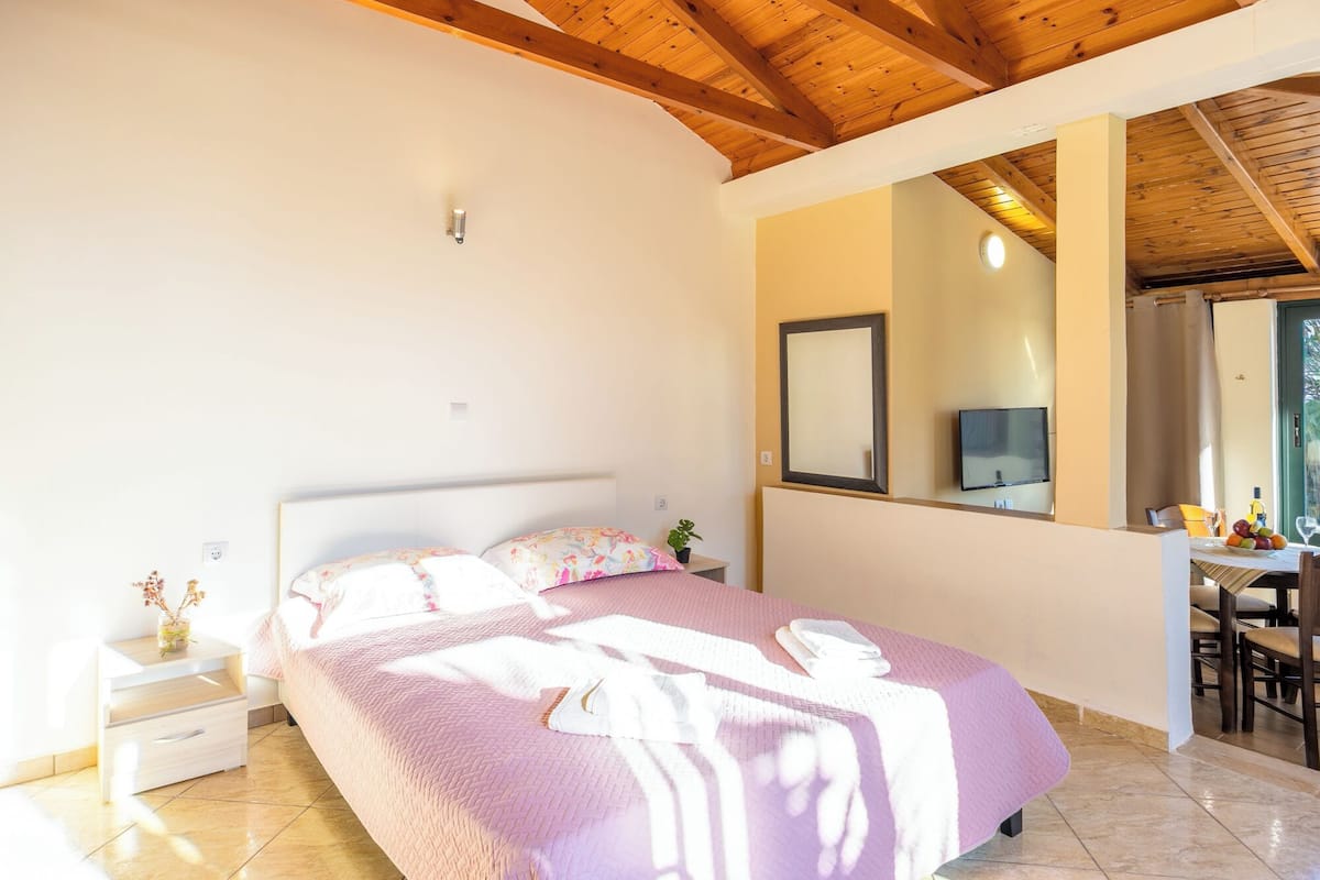 A bedroom with a bed, bedside table, mirror, and a small desk with a chair.