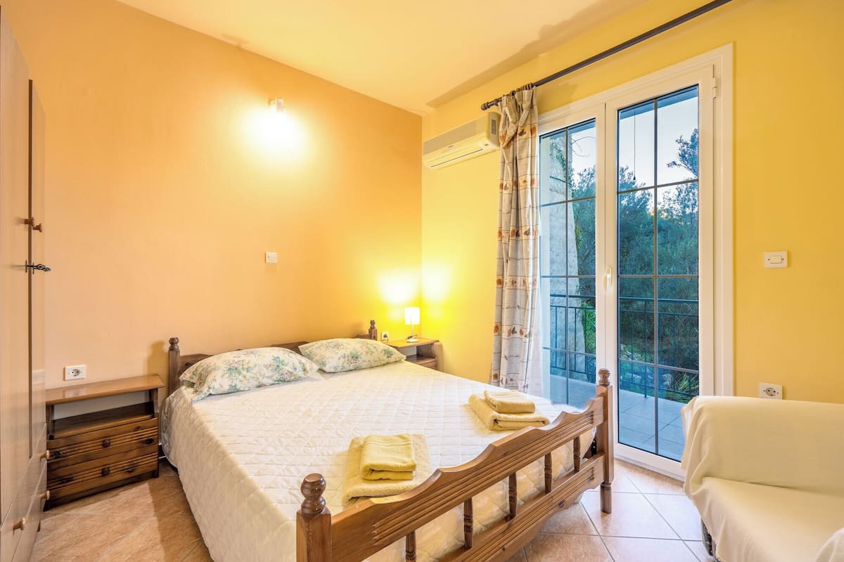 A bedroom with a bed, bedside lamps, a chair, and a view through a window.