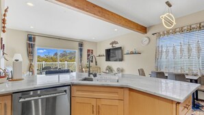A modern kitchen with a large island, wooden cabinets, stainless steel appliances, a dining area with a table and chairs, and a balcony with a view. - Lakeview Home steps away Twin Rocks Beach Access (Rockaway Beach)