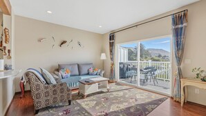 A living room with a sofa, coffee table, and a view of a deck and mountains. - Lakeview Home steps away Twin Rocks Beach Access (Rockaway Beach)