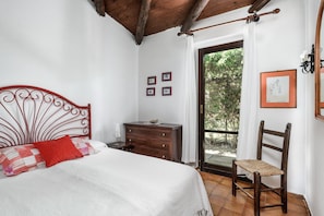 A bedroom with a bed, a wooden dresser, a chair, and a window with a view of greenery.