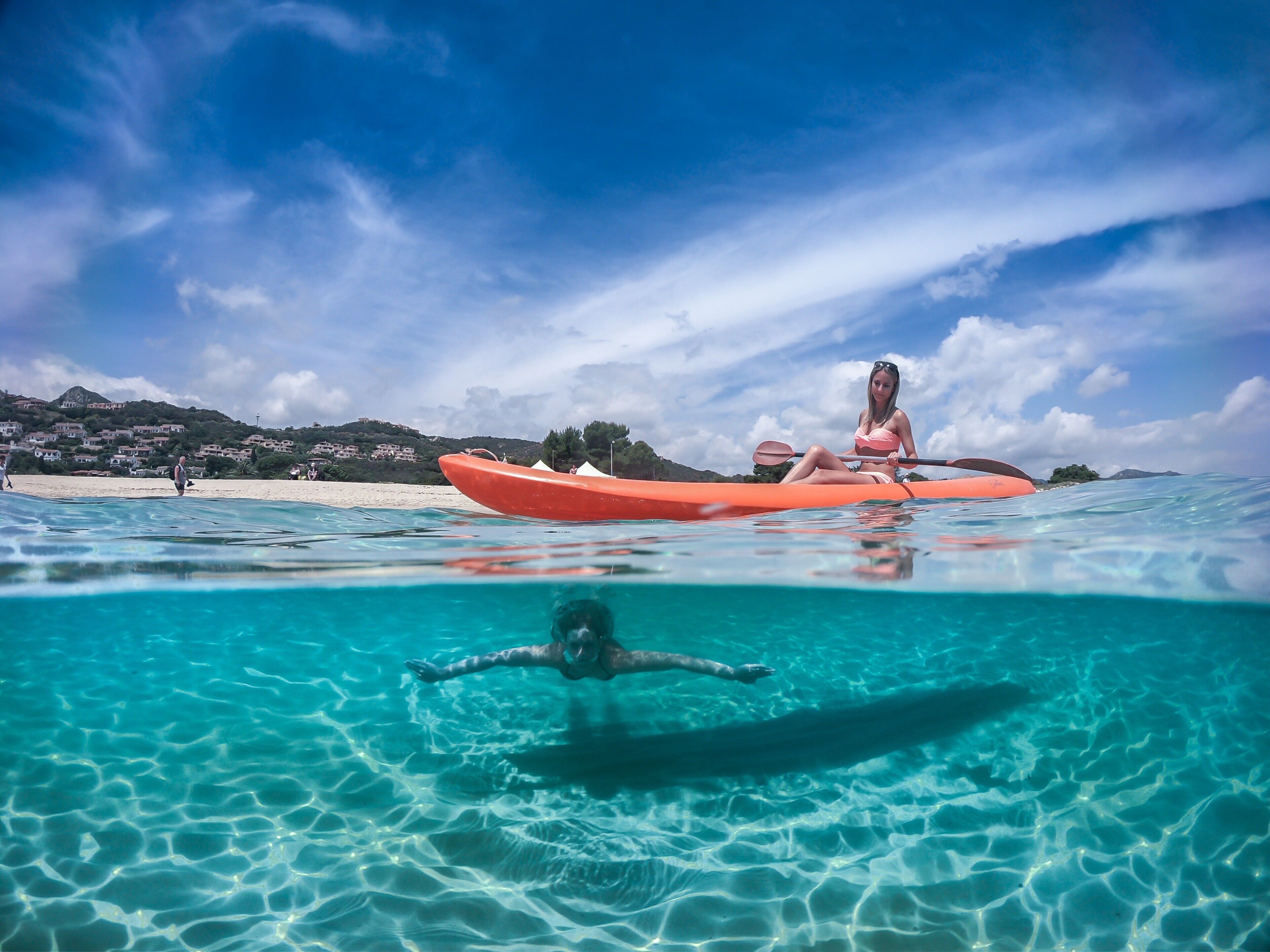 A clear blue sea with a person kayaking and another swimming underwater.