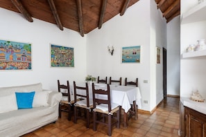 A dining area with a wooden table and chairs, a sofa with a blue pillow, and wall art.
