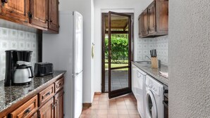 A compact kitchen with wooden cabinets, a coffee maker, a toaster, and a washing machine. - Villa Romana – Beach House with Fenced Garden at Costa Rei (Costa Rei)