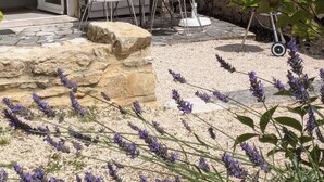 Un área de estar al aire libre con muros de piedra, un paraguas rojo y plantas de lavanda.