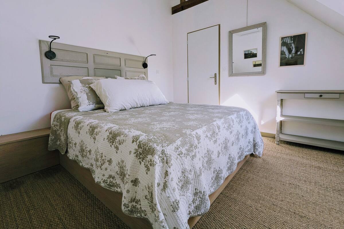 A bedroom with a bed, a dresser, a door, and a wall-mounted mirror.