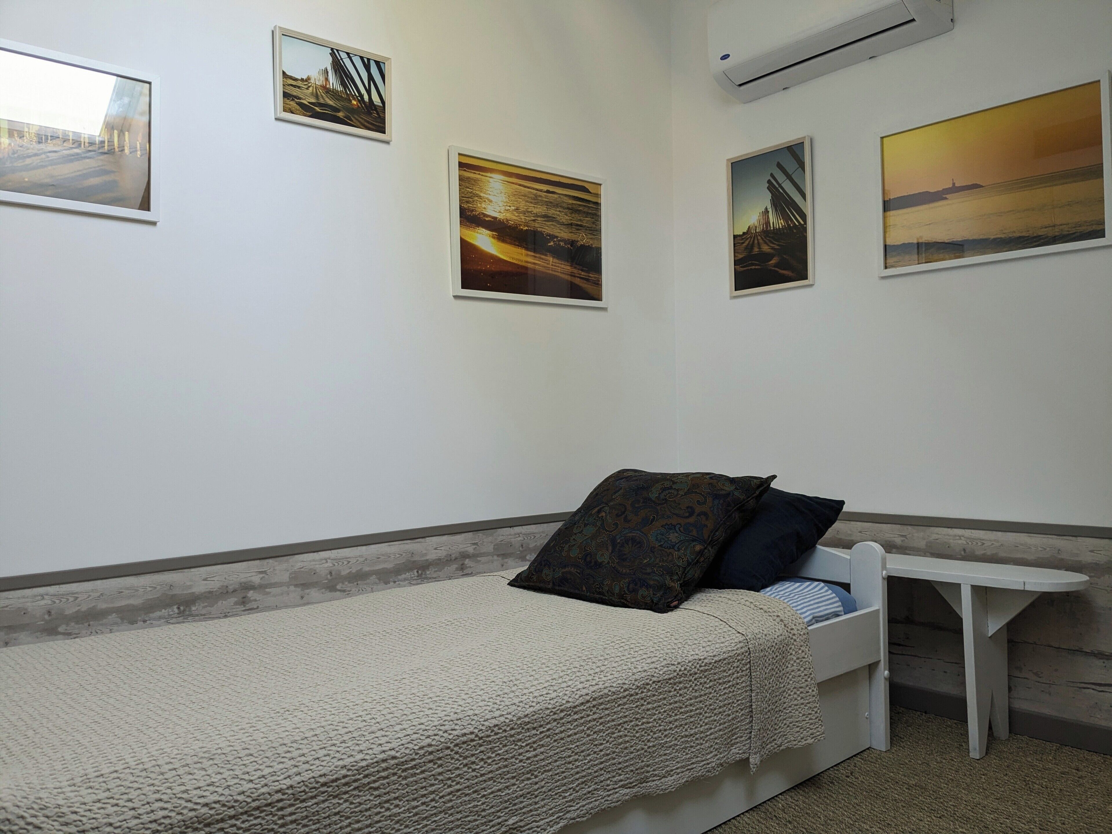 Una cama individual con una colcha texturizada, una mesita de noche y tres cuadros enmarcados en la pared.