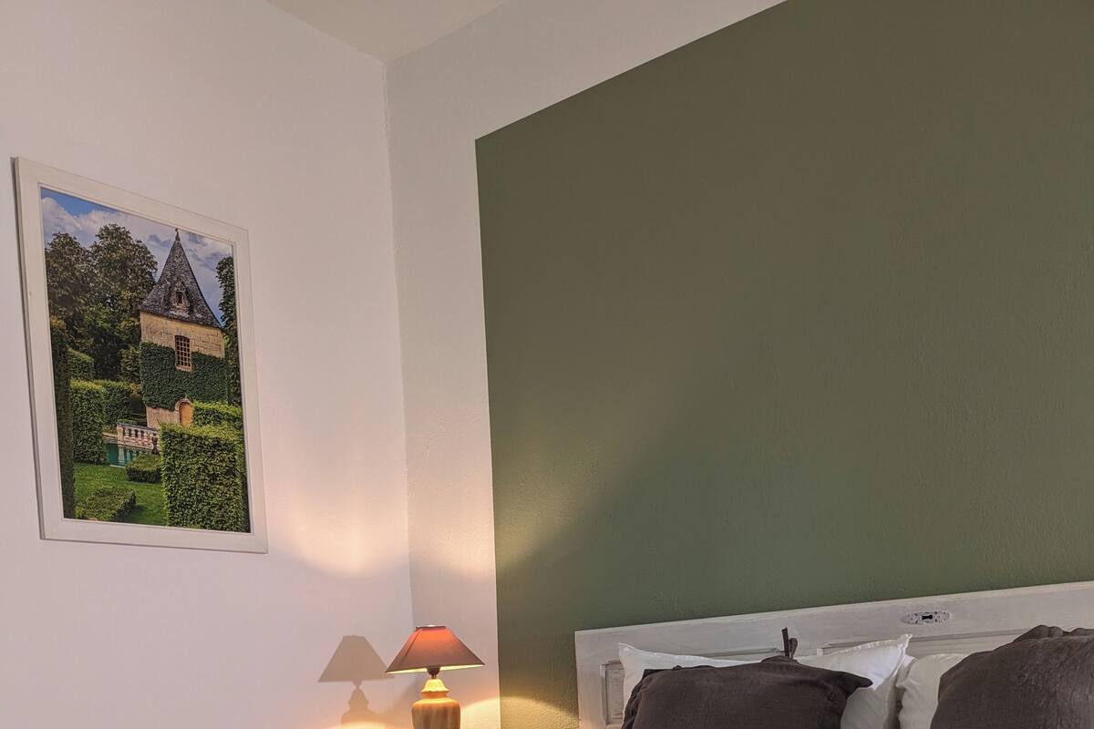 A neatly made bed with a green blanket, a bedside lamp, and a framed picture on the wall.