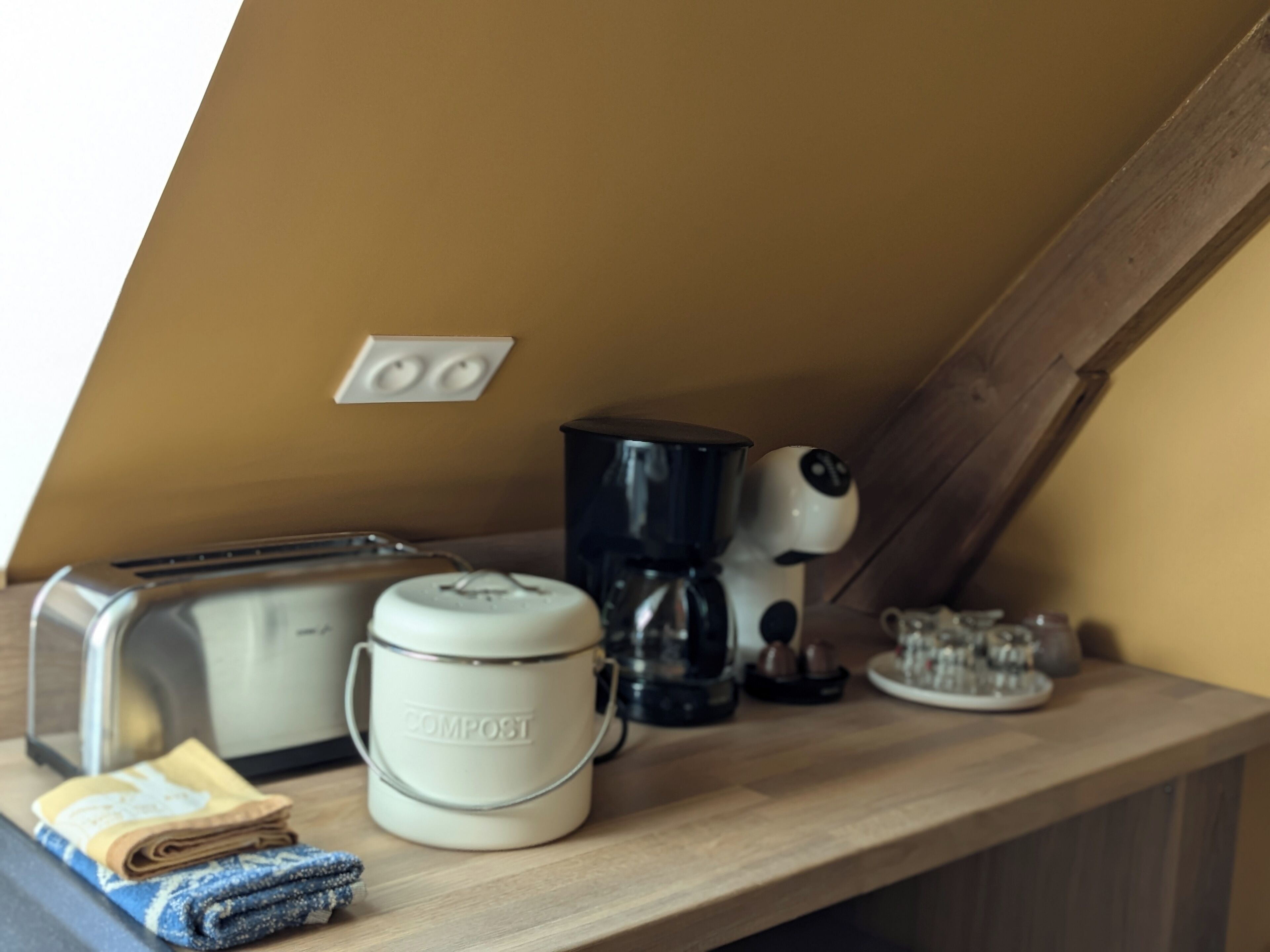A kitchen counter with a toaster, a coffee maker, a compost bin, and a kettle.