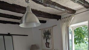 Una habitación acogedora con techo de madera, un sofá blanco, una mesa de centro de madera con tazas y una tetera, y vistas a zonas verdes al exterior.
