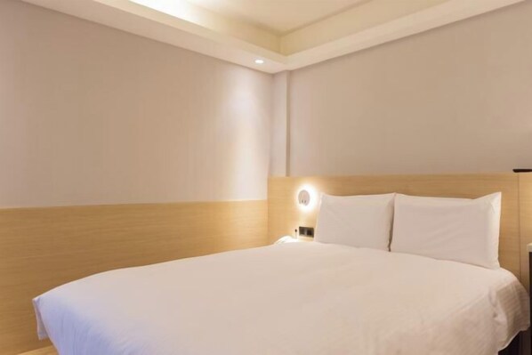 Une chambre d’hôtel avec un grand lit, une table de chevet et une lampe fixée au mur.