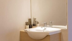 A modern bathroom with a large white sink, two faucets, and a mirror above it.