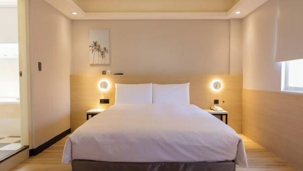 A modern hotel room with a large bed, bedside tables, and a ceiling light fixture.
