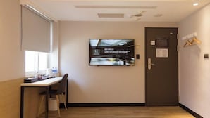 A hotel room with a desk, chair, and a television mounted on the wall.