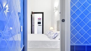 Quarto de hotel com uma cama, mesa de cabeceira, luminária na parede e porta com um aviso de boas-vindas.