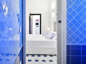 Une chambre d’hôtel avec un lit, une table de chevet, une lampe fixée au mur et une porte ornée d’une pancarte de bienvenue.