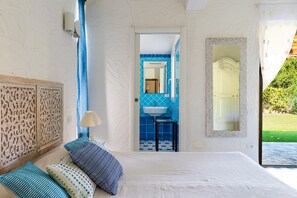 Ein Schlafzimmer mit Bett, Kissen, einer Lampe, einem Spiegel und einem durchgegangenen Tür erkennbaren Badezimmer.