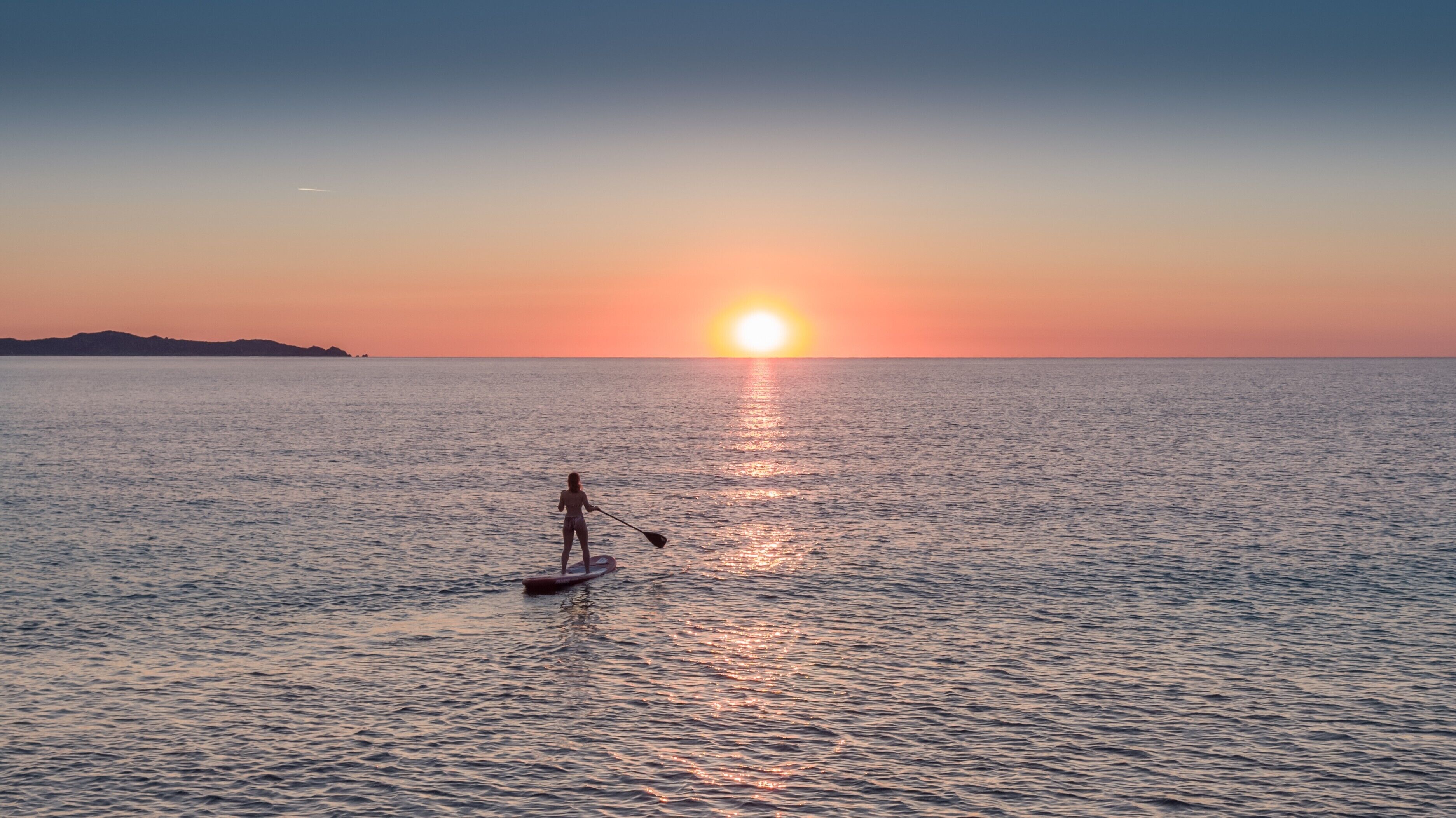 Iemand staat op een paddleboard op kalm water tijdens de zonsondergang.