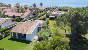Uma área residencial costeira com casas de telhas de barro, gramados verdes e uma vista clara do mar.