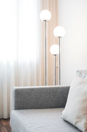 A room with a grey sofa, two tall floor lamps with round shades, and a window with sheer curtains. - Urban Retreat w/ Balcony | Bright & Central Porto (Porto)