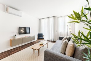 A modern living room with a flat-screen TV, a sofa, a chair, a wooden coffee table, and a large window with curtains. - Urban Retreat w/ Balcony | Bright & Central Porto (Porto)