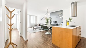 A modern kitchen with a central island, a dining area with a round table and chairs, and a living room with a sofa and a TV. - Urban Retreat w/ Balcony | Bright & Central Porto (Porto)