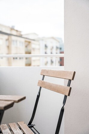 A chair with a wooden backrest and metal frame, positioned on a balcony with a view of buildings in the background. - Urban Retreat w/ Balcony | Bright & Central Porto (Porto)