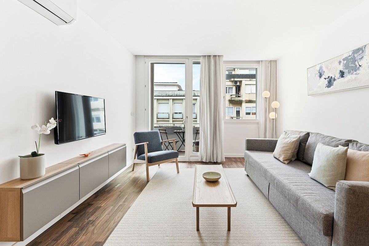 A modern living room with a sofa, a coffee table, a TV, and a view of the city through large windows.