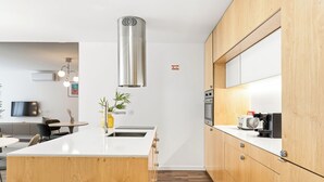 A modern kitchen with a central island, wooden cabinets, stainless steel appliances, and a pendant light. - Urban Retreat w/ Balcony | Bright & Central Porto (Porto)