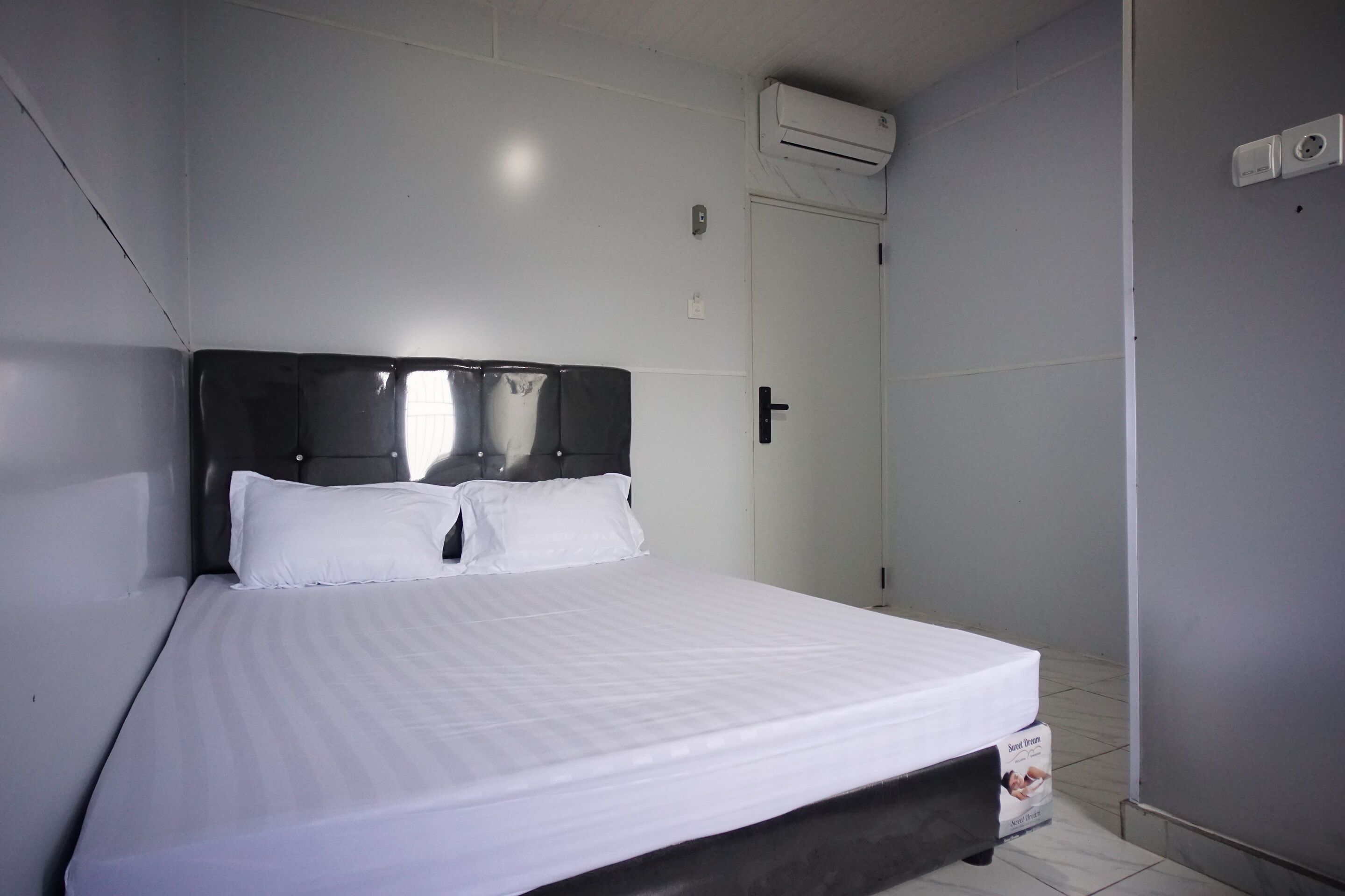 A neatly made bed with a dark headboard, a white wall, and a door with a handle.